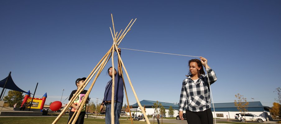 A photo of three people erecting a tipi.