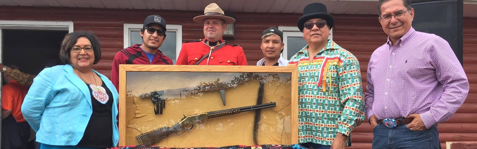 A photo of Roxanne Tootoosis, Jordan Tootoosis, Corporal Lefevbre, Lakota Tootoosis, Councilor Milton Tootoosis and Blaine Favel posing with Poundmaker’s Winchester gun and his staff, which went on display at Poundmaker Museum.