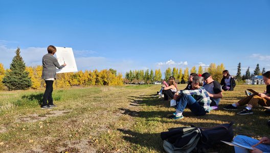 A photo of artist Bonny Kendel-Macnab guiding an art-making activity in front of a group of young students, out in nature.