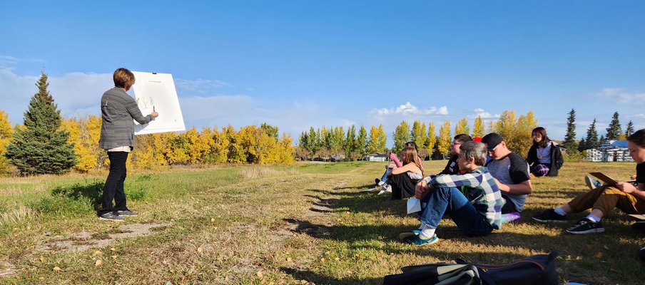 A photo of artist Bonny Kendel-Macnab guiding an art-making activity in front of a group of young students, out in nature.