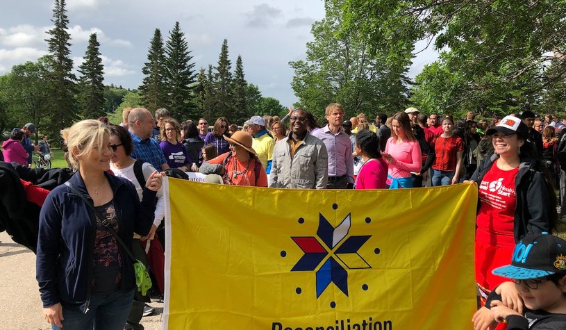 A photo of a crowd of people holding up a Reconciliation flag in an event supported by funding from the Multicultural Initiatives Fund.