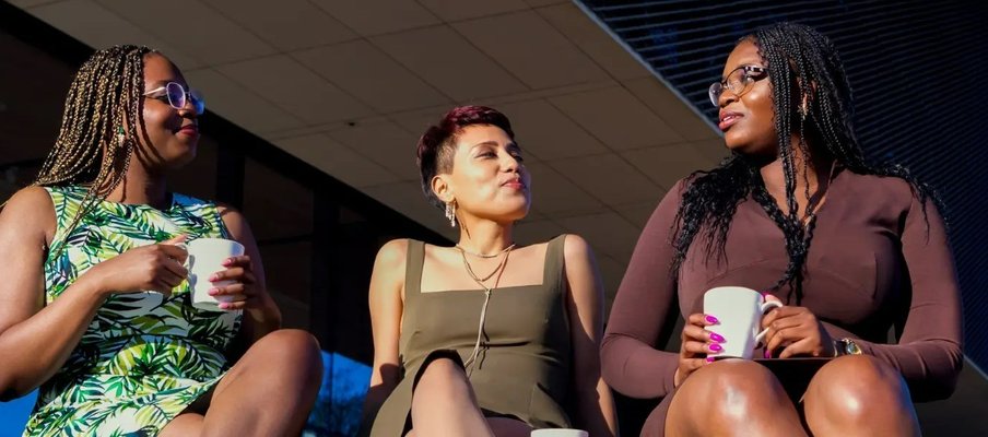 A photo of the directors of BIPOC Coffee Talk Inc. (Theresa Quagraine, Dyana Castillo, and Theodocia Quagraine) sitting together, holding mugs.