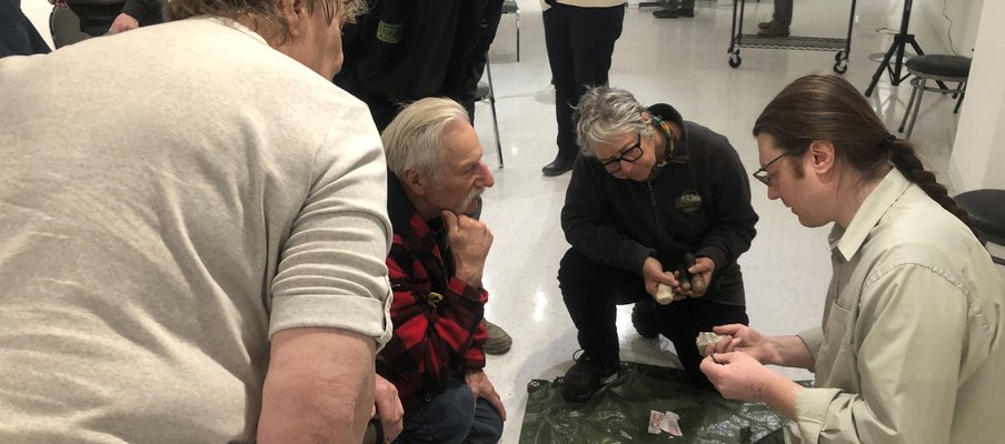 A photo of Gabriel Essaunce Lemarche, from SAS, doing a flintknapping demonstration with a small group.