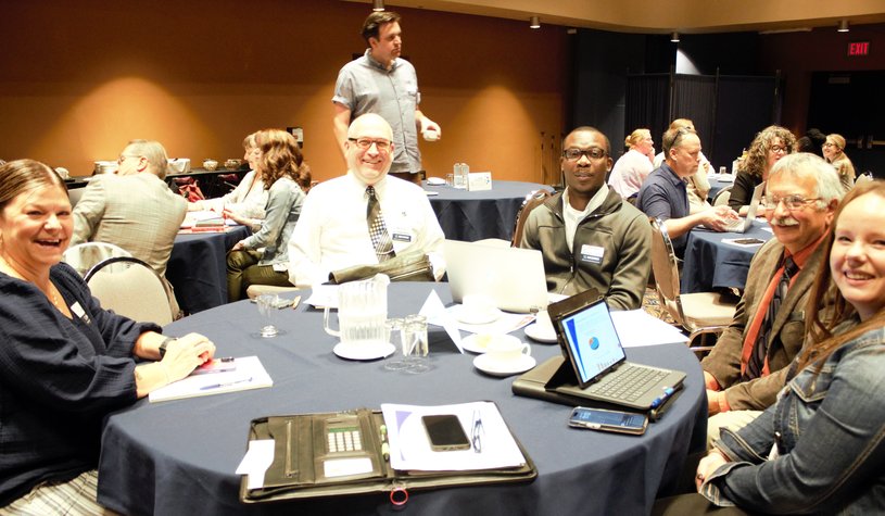 A photo of people sitting around a table at the 2023 AGM, smiling at the camera.