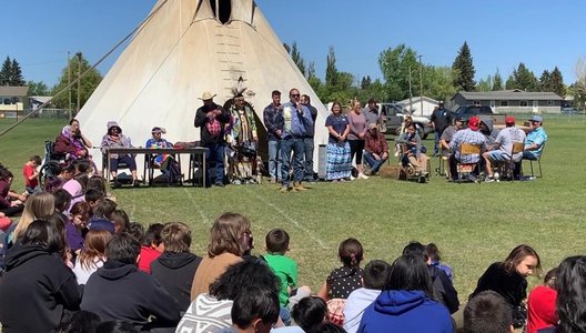 A photo of a person addressing a crowd of students at a pow wow.