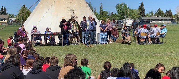 A photo of a person addressing a crowd of students at a pow wow.