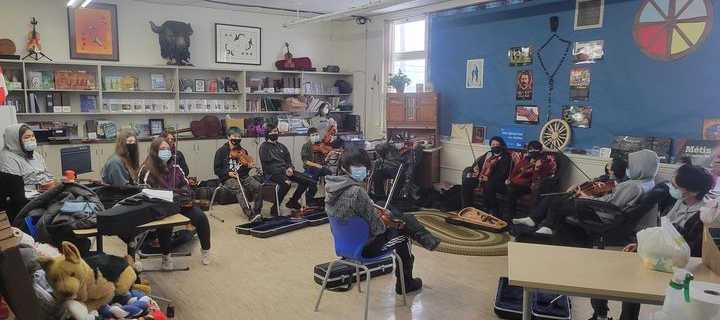 A photo of kids in a classroom learning to play the fiddle.