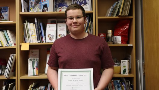 A photo of German language student Ethan holding up his award diploma.