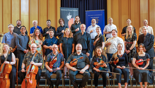 a photo of a group of orchestra members sitting and holding violins