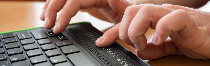 Hands using a braille display keyboard reflecting the use of assistive technology for visually impaired users.