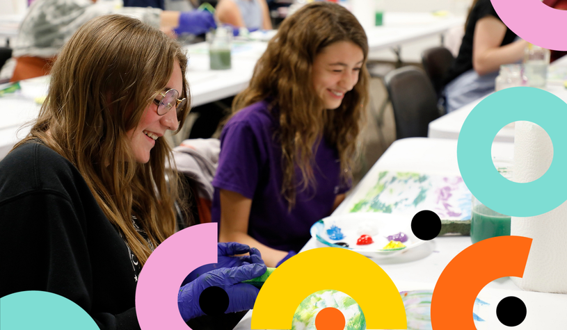 A photo of two people smiling, sitting at a table with paper and paints, at a Culture Days event.