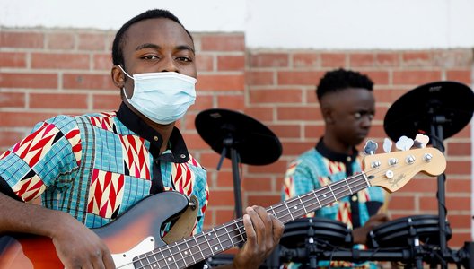 Two musicians playing the guitar and drums at the YWCA Re:Imagine Fashion event in 2021 for Culture Days. The one closest to the camera is wearing a face mask.