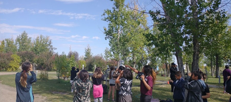 A photo of young students looking around them with binoculars in a park as part of the NatureHood Program.