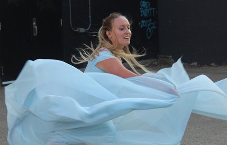 dancer in swirling white fabric against a backdrop  of an alley mural of a whale