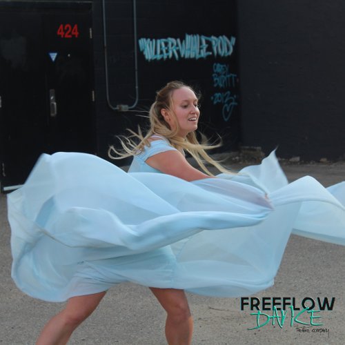 dancer in swirling white fabric against a backdrop  of an alley mural of a whale