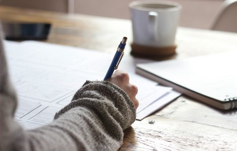 A hand holds a pen and is ready to write on a piece of paper.