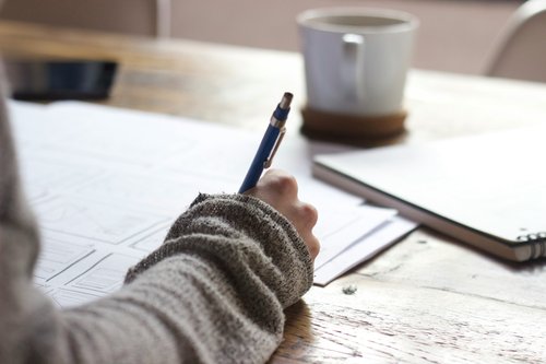 A hand holds a pen and is ready to write on a piece of paper.